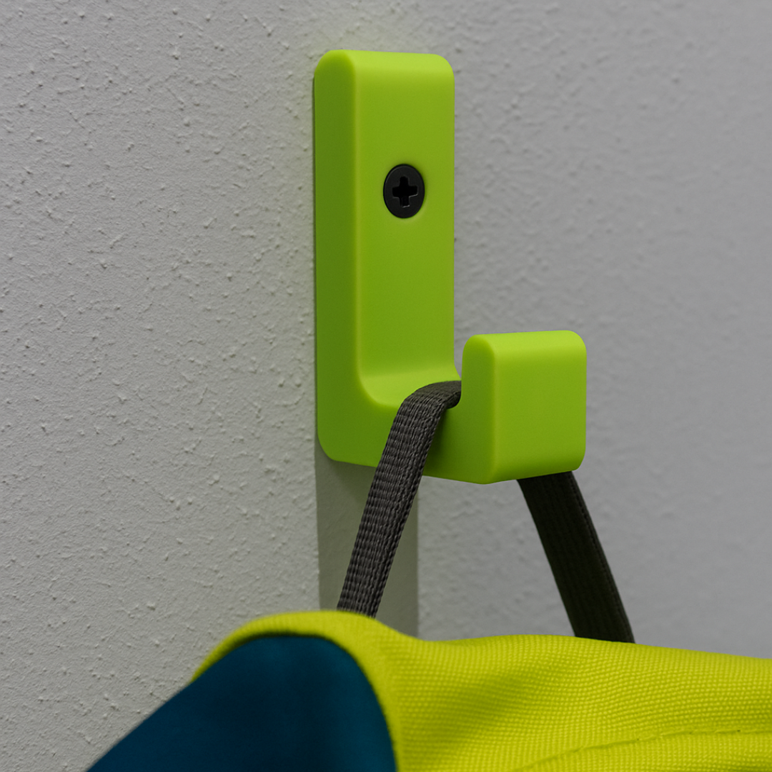 Ein limegrüner, 3D-gedruckter Wandhaken aus PLA ist an einer hellgrauen Wand montiert und hält den Trageriemen eines Rucksacks. Das Bild zeigt den Haken in einem realistischen Anwendungsszenario und dient als Werbemotiv für die Produktkollektion.
