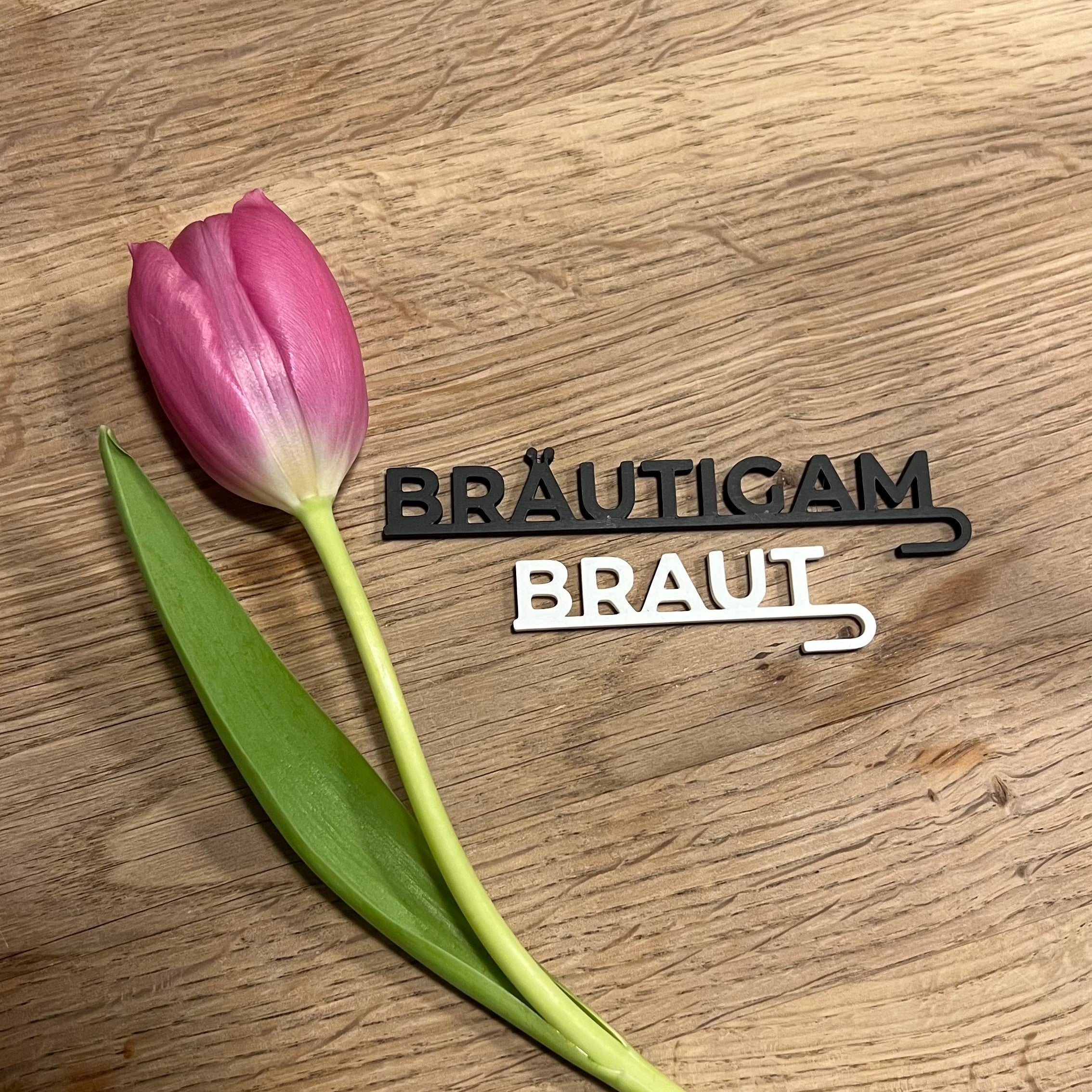 „Nachhaltige 3D-gedruckte Glasanhänger „Braut“ und „Bräutigam“ aus PLA für Hochzeitsgläser dekoriert neben einer Tulpe. Schlichte, elegante Anhänger in Weiß und Schwarz, perfekt für jede Hochzeitsdeko. Diese personalisierten Anhänger verleihen Braut- und Bräutigamsgläsern einen besonderen Touch und passen sich harmonisch verschiedenen Hochzeitsstilen wie Boho, Vintage oder Modern Chic an. Ein umweltfreundliches und elegantes Geschenk zur Hochzeit, das für einen persönlichen Akzent sorgt.“