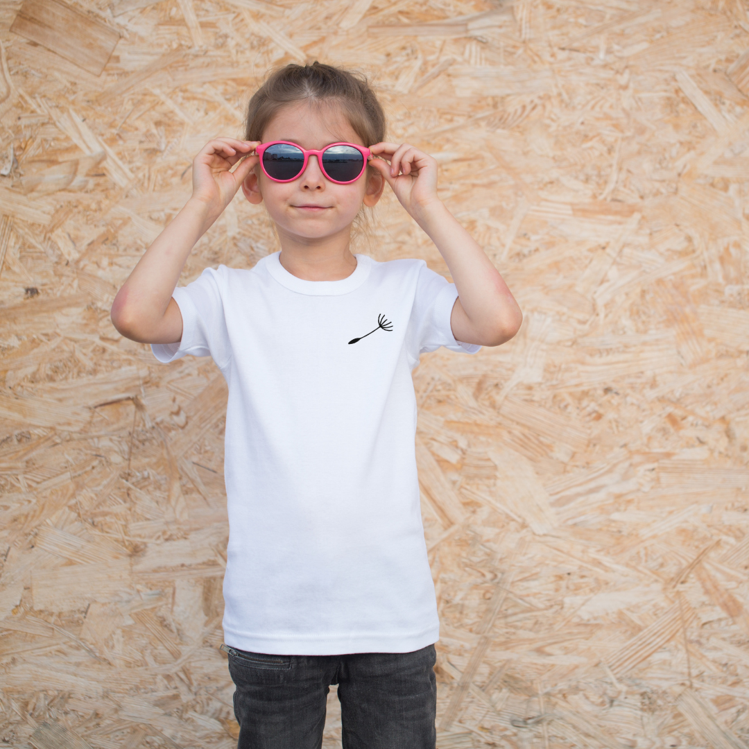 Mama-Kind-Shirt-Set aus Bio-Baumwolle mit Pusteblumen-Design: Auf dem taillierten Mama-Shirt fehlt ein Schirmchen, das auf dem Kind-Shirt einzeln erscheint. Symbol für Liebe, Verbindung und Loslassen. Die Shirts liegen auf natürlichem Hintergrund, modern und nachhaltig inszeniert. Ideal als Muttertagsgeschenk, zur Geburt oder für emotionale Familienmomente. Hier Kindershirt in weiß angezogen.