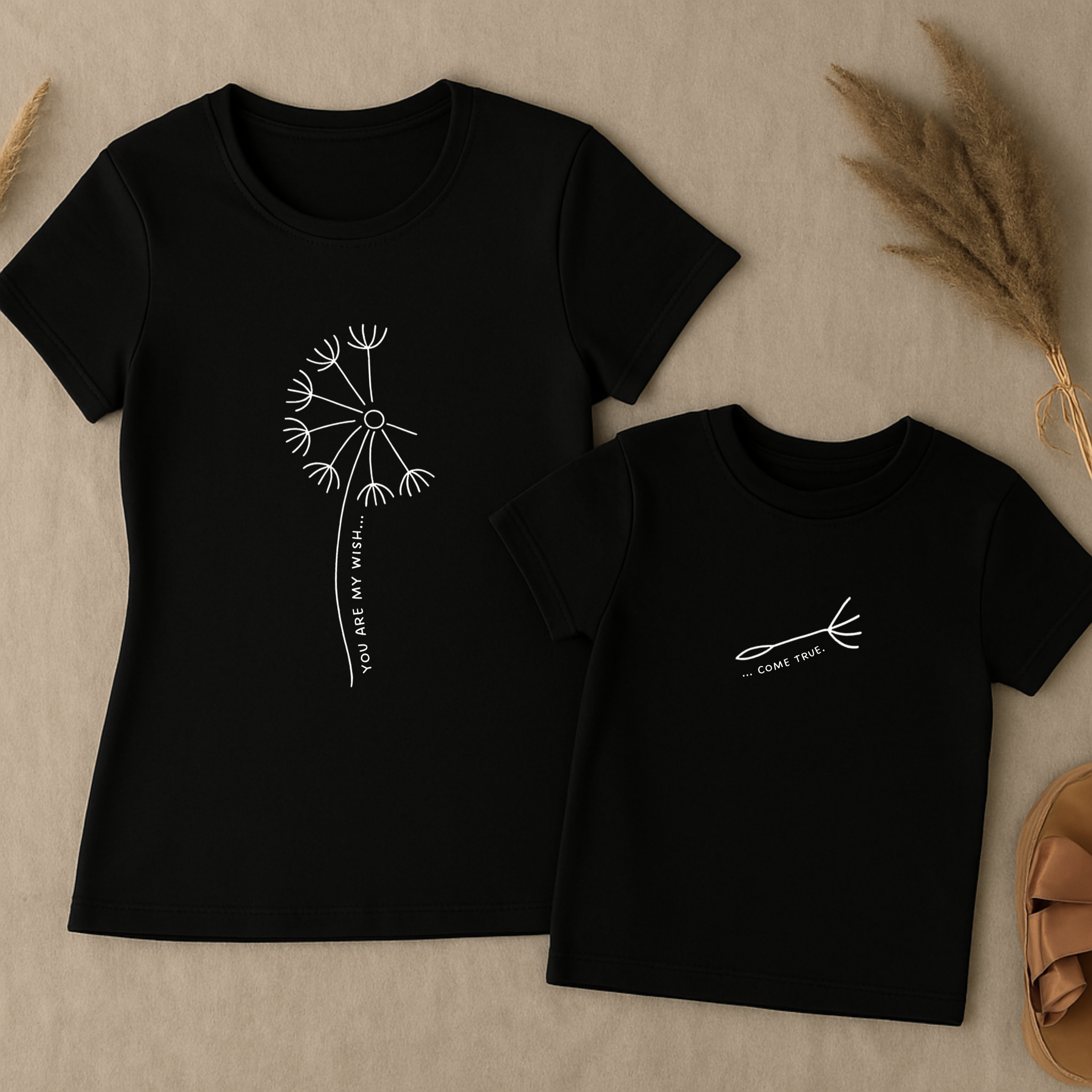 Mama-Kind-Shirt-Set aus Bio-Baumwolle mit geteiltem Spruch: „You are my wish … come true“. Schwarzes T-Shirt für Mama mit Pusteblume und fehlendem Schirmchen, passendes Kind-Shirt mit einzelner Pusteblumenschirmchen-Grafik. Hochwertig, nachhaltig, ideal als Muttertagsgeschenk, zur Geburt oder für Familienfotos. Perfektes Geschenk für Mamas und Kinder – liebevoll, modern und emotional gestaltet.